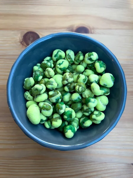 Close up shot of a blue ceramic code filled with wasabi covered peas in a japanese restaurant. Green wasabi on green peas, very spicy starter or appetizer to share. Wooden background.