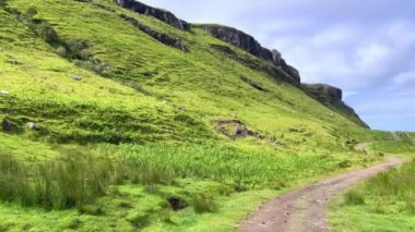 Wide angle 4k footage with camera panning along the grassy peaks, fields and the blue sea and black rocks of Talisker Bay, in Skye Island. Waterfall ending in the sea. Beach and mountain scapes.
