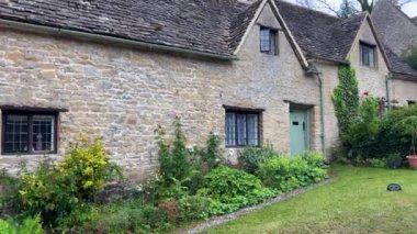 Wide angle shooting of the charming row of typical cotswold cottages in the historic village of Bibury, Gloucestershire. Fairy tale stone houses decorated with plants and flowers.