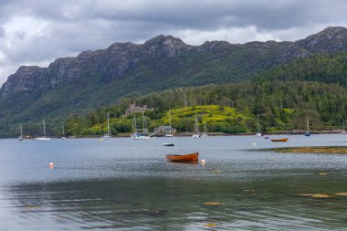Scenic waterfront views of beautiful Plockton with its tranquil loch with wooden boats in the middle. Scottish coastal touristic destinations.