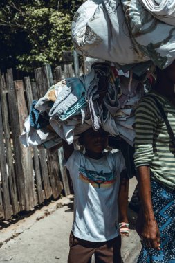 Pedernales, Dominican Republic, 22 august 2022. Portrait of an Haitian lkid walking with piles of rags and linens on their heads towards the selling zone. Sadness, misery on his face.