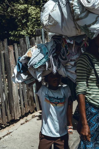 Pedernales, Dominican Republic, 22 august 2022. Portrait of an Haitian lkid walking with piles of rags and linens on their heads towards the selling zone. Sadness, misery on his face.