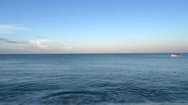 Static camera on the wonderful sea of Playa de la Cueva de las Aguilas, Pedernales, Dominican Republic, as a fishermens boat passes in the frame, from right to left, in the gentle sunrise light. 