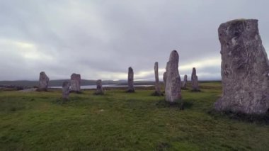 Bulutlu bir akşamda Callanish ya da Calanais taş çemberinin ayakta duran taşları ya da megalithleri etrafında hareket ediyorlar. Güneş kutunun içinden bakıyor, büyü, antik, neolitik atmosfer. Arkeolojik alanlar.
