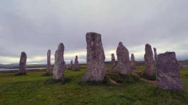 Bulutlu bir akşamda Callanish ya da Calanais taş çemberinin ayakta duran taşları ya da megalithleri etrafında hareket ediyorlar. Güneş kutunun içinden bakıyor, büyü, antik, neolitik atmosfer. Arkeolojik alanlar.