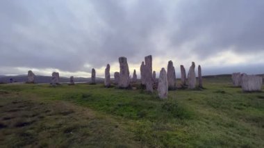 Bulutlu bir akşamda Callanish veya Calanais taş çemberinin ayakta duran taşlarına doğru yürüyorlar. Güneş kutunun içinden bakıyor, büyü, antik, neolitik atmosfer. Arkeolojik alan