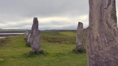 Bulutlu bir akşamda Callanish ya da Calanais taş çemberinin ayakta duran taşları ya da megalithleri etrafında hareket ediyorlar. Güneş kutunun içinden bakıyor, büyü, antik, neolitik atmosfer. Arkeolojik alanlar.