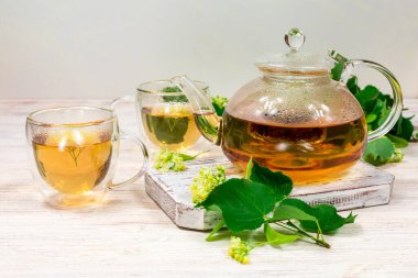 Çaydanlık ve ahşap bir masanın üzerinde ıhlamur ağacı olan iki fincan çay. Çay demliyorum..