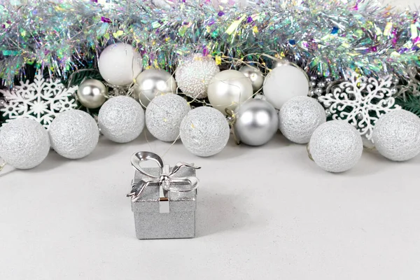 Zilverkleurige geschenkdozen op een wazige achtergrond met witte en zilveren ballen, slinger en knutsel. Kerstkaart met witte en zilveren ballen, slinger, knutsel, sneeuwvlokken op een wazig witte achtergrond. — Stockfoto