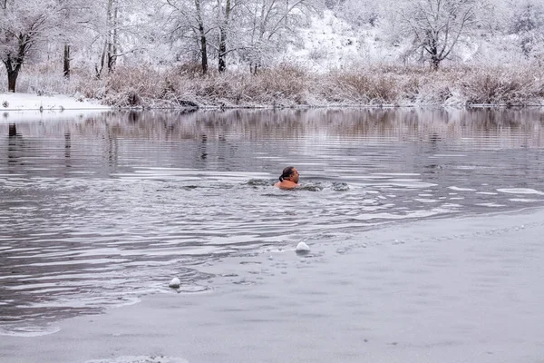 A middle-aged man swims on a cold winter day along the river against the backdrop of snow-covered trees. The concept of hardening, healthy lifestyle — 스톡 사진