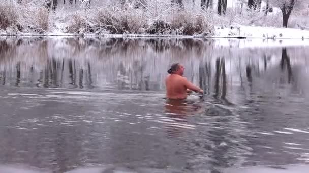 한 중년 남자가 겨울 강에서 눈덮인 나무들을 배경으로 수영을 한 후 물에서 나온다. 단단 해 지는 개념, 건강 한 생활 방식 — 비디오