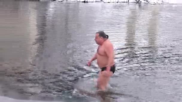 Człowiek wychodzi z wody po kąpieli w zimowej rzece na tle zimowego lasu. — Wideo stockowe