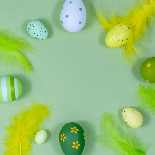 Hermoso marco de Pascua festivo hecho de huevos de colores, plumas sobre un fondo verde. Copia el espacio para tu diseño. Vista desde arriba. Lugar para el texto. — Foto de Stock