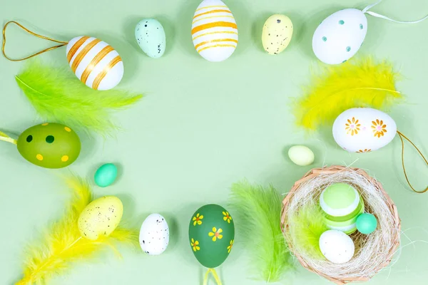 Marco de Pascua con huevos, plumas y un nido sobre un fondo verde. Concepto mínimo. Vista desde arriba. Tarjeta con espacio de copia para texto. — Foto de Stock