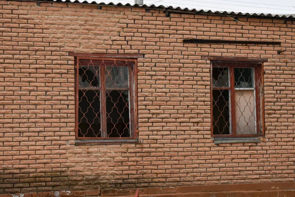 Zwei zerbrochene Fenster mit einem alten Holzrahmen an der Ziegelwand des Hauses nach der Explosion. — Stockfoto