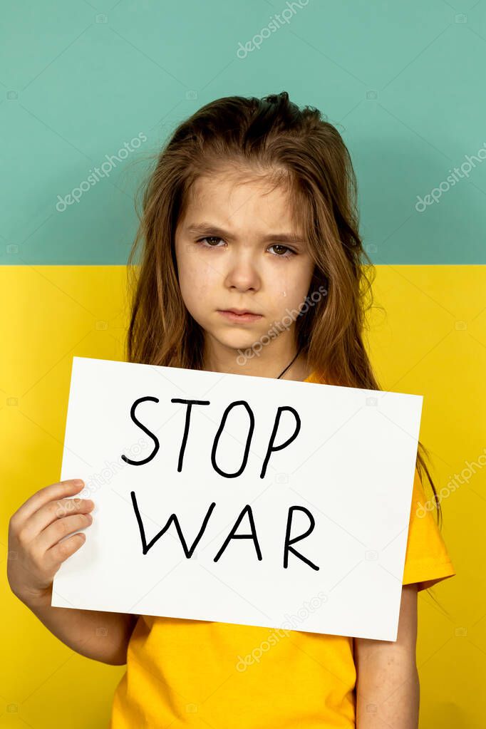A girl is crying, holding a STOP poster on the background of the Ukrainian flag. Stop the war in Ukraine. The concept of peace in Ukraine.
