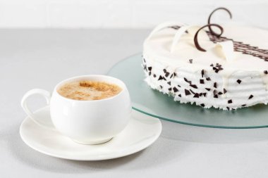 Bir fincan kahve ve gri arka planda cam bir tabakta çikolata dekoru ile süslenmiş beyaz bir pasta. Seçici odak.