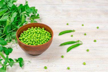 Beyaz ahşap arka planda bir kasede taze yeşil bezelyeler. Düzgün beslenme, vitaminler. Yakın plan. Seçici odak.