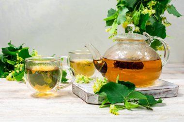 Çaydanlık ve iki fincan çay, ahşap bir masada ıhlamur ağacı..