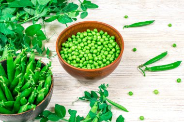 İki kase taze taze taze bezelye dikişli ve yaprak filizlerinin arka planında soyulmuş, beyaz ahşap bir masada taze yeşil bezelye dalları.