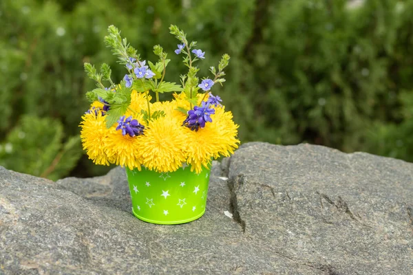 Bouquet of dandelions and blue flowers in a bucket on a stone. Dandelion flowers. Copy space. Place for an inscription. Selective focus