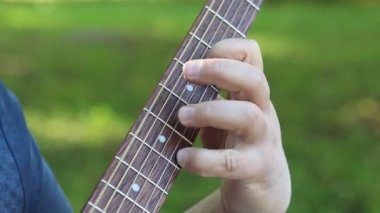 Elleri dışarıda oynayan bir gitaristin ellerinin yakın çekimi. Gitarist dışarıda parkta gitar çalar.