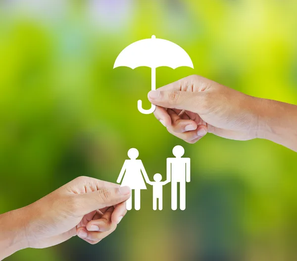 Mano sosteniendo una familia de papel y paraguas sobre fondo verde, concepto de seguro Fotos De Stock Sin Royalties Gratis