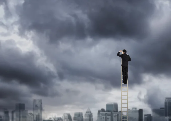 Empresário subindo em uma escada sobre uma cidade olhando para a frente — Fotografia de Stock