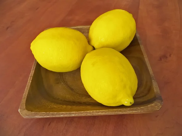 Tres limones frescos en un plato de madera — Foto de Stock