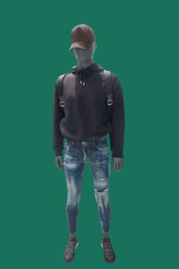 Yeşil arka planda kahverengi kapüşonlu ve yırtık kot pantolonlu bir erkek vitrin mankeni.