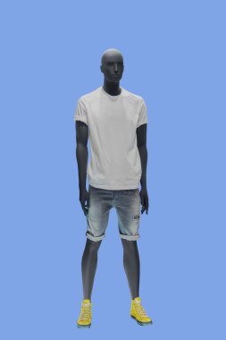 Mavi arka planda beyaz tişört ve yırtık kot pantolon giyen bir erkek vitrin mankeni.