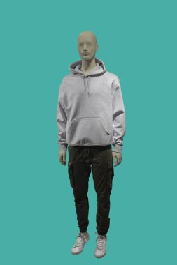 Yeşil arka planda izole edilmiş gri kanguru cep kapüşonu giyen bir erkek vitrin mankeni.