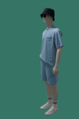 Yeşil arka planda izole edilmiş yaz tişörtü ve şort giymiş bir erkek vitrin mankeni.