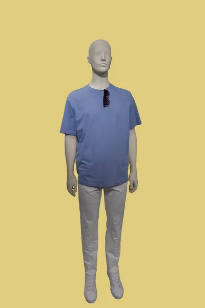 黄色の背景に隔離された青のTシャツと白いズボンを身に着けている男性ディスプレイマネキンの完全な長さの画像 — ストック写真