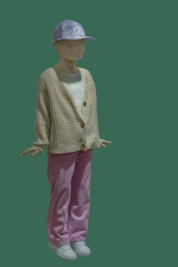 Örgü ceket ve yeşil arka planda izole edilmiş pembe kot giyen bir çocuk mankeninin tam boy görüntüsü