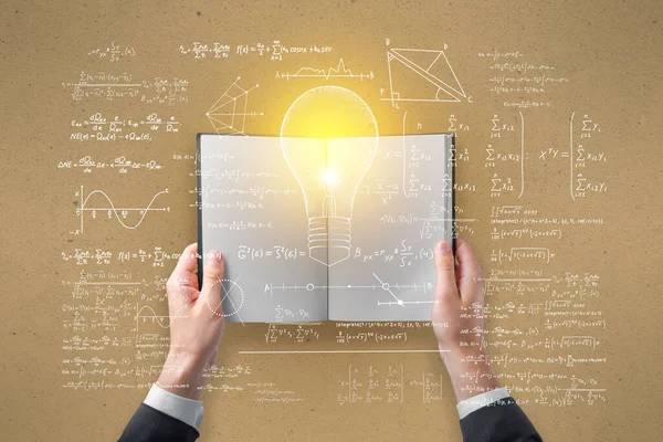 Hand holding open book with abstract light bulb sketch with mathematical formulas on light wall background. Intelligence, idea, solution, science and innovation concept