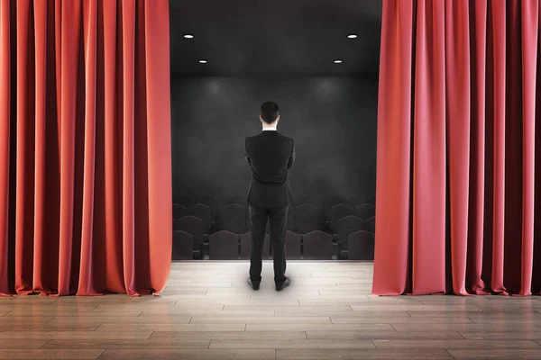 赤いカーテンの後ろからステージを見てビジネスマンのバックビュー エンターテイメント パフォーマンス プレゼンテーションのコンセプト — ストック写真