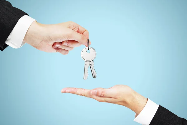 Close up of businessperson handing keys on blue background. Housing, property, investment and purchase concept