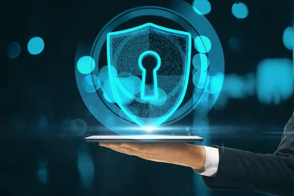Close up of businessman hand holding tablet with glowing shield and padlock hud on blurry background. Safety and security concept. Double exposure