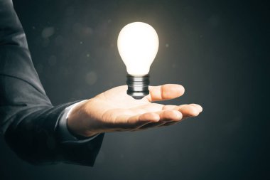 Close up of businessman hand holding glowing light bulb. Idea and innovation concept clipart