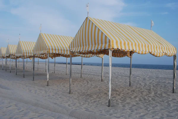 Yellow striped tents lined up on beach with ocean in background