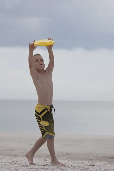 Ung pojke streatching att fånga en gul disk på stranden — Stockfoto