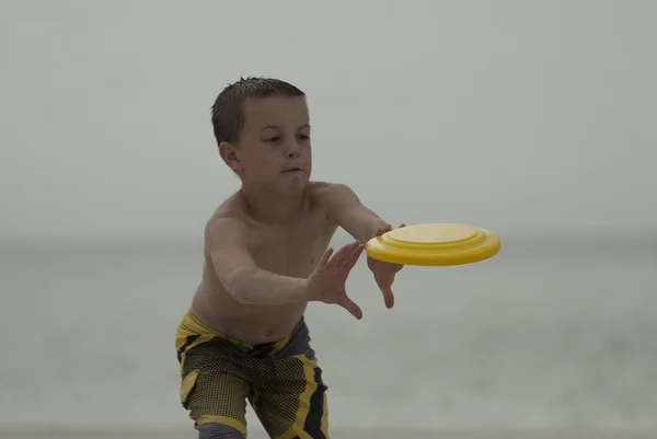Ung pojke att nå för att fånga en gul disk på stranden — Stockfoto