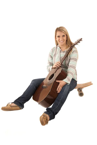 Smiling woman sitting on skate board with guitar — Stock Photo, Image
