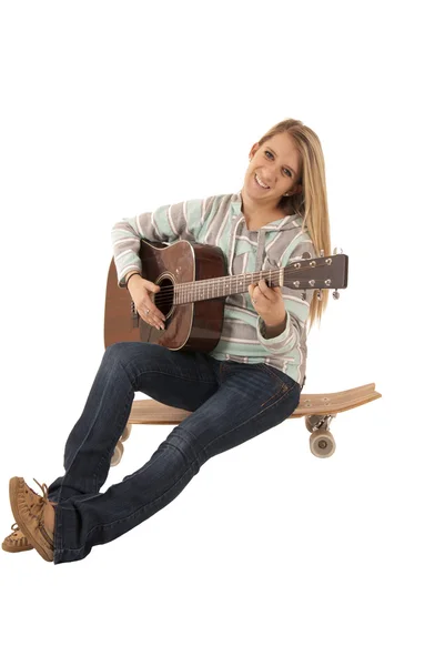 Atractive woman sitting on skate board playing guitar — Stock Photo, Image