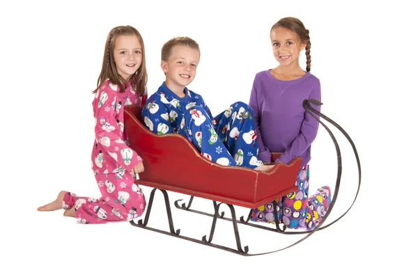 Three children in winter pajamas around a sleigh — Stock Photo, Image