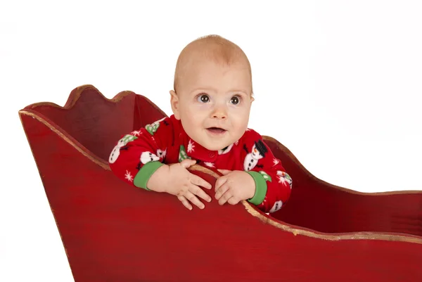 Toddler boy in red christmas pajamas in a red sleigh — Stock Photo, Image