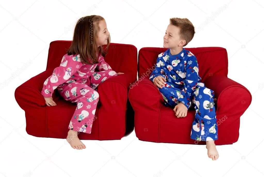two children laughing wearing winter pajamas sitting in red chai