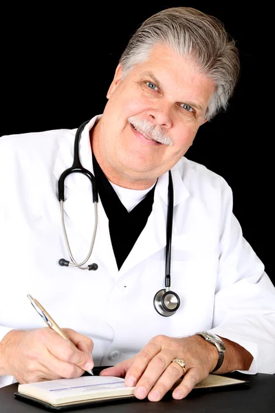 Красивый зрелый голубоглазый врач, улыбающийся, пишущий прескри — стоковое фото