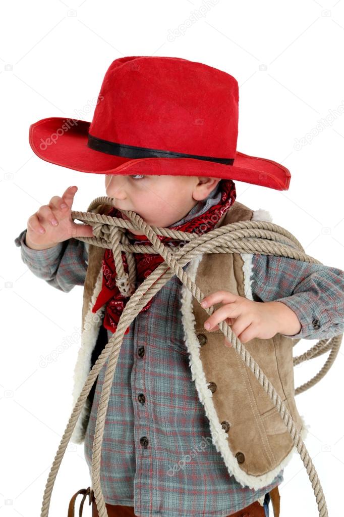 Cute young cowboy toddler biting a rope wearing red hat